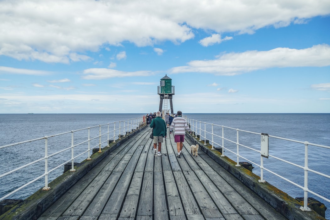 Man walking down ax pier with blue sea surrounding it