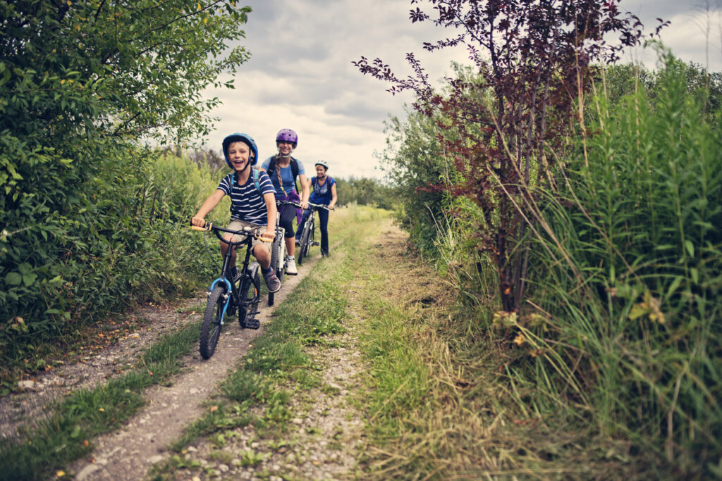 Kids with mother riding bicycles in nature. Kids are smiling happily.